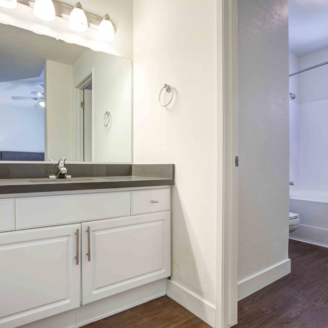 Stoneridge – Modern bathroom with a wide vanity featuring white cabinetry, dark countertops, and a large mirror