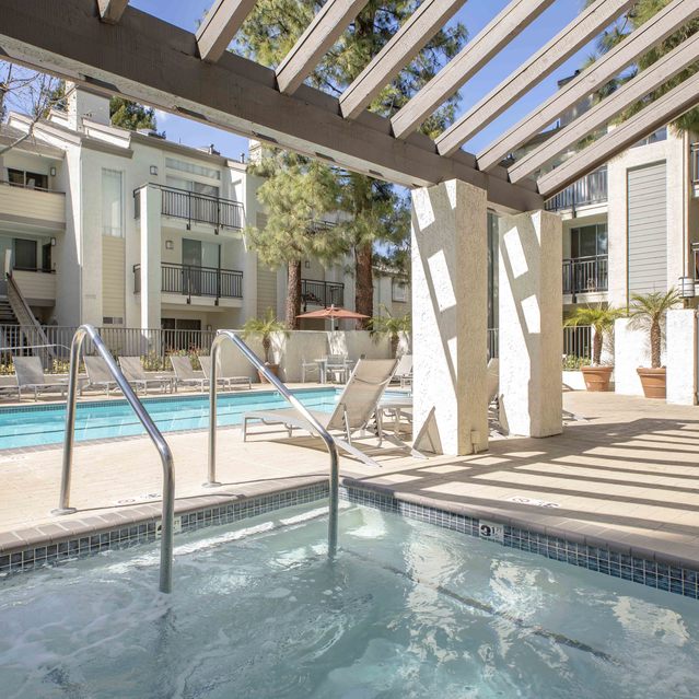Stoneridge – Outdoor spa with clear water under a modern pergola, featuring metal handrails surrounded by light stone decking