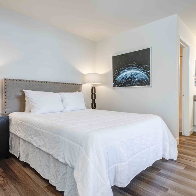 Stoneridge – Modern bedroom with a neatly made bed featuring a white comforter and upholstered headboard