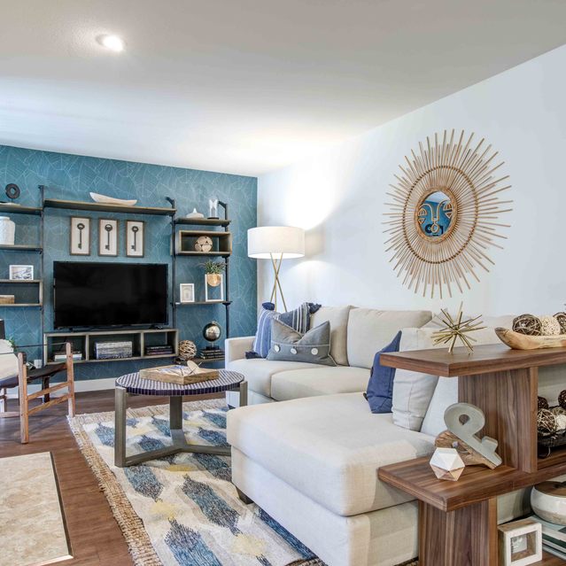 Stoneridge – Stylish living room with a large cream sectional sofa accented by blue and patterned throw pillows, a modern wooden