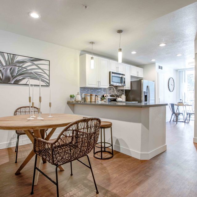 Stoneridge – Open dining area with a round wooden table and two modern wire-frame chairs, accented by a cushioned bench